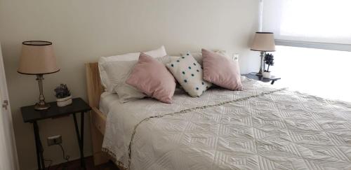 Un dormitorio con una cama con almohadas rosas y blancas. en Departamento en Bosques de Montemar, en Concón