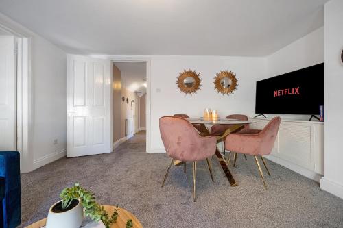 a dining room with a table and two pink chairs at Cotswolds- 2 bed flat in 18th Century building, town centre with Smart TV - Esho Stays in Cirencester