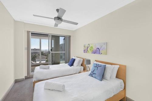 two beds in a room with a ceiling fan at Sandy Cove Apartment The Entrance 22 in The Entrance