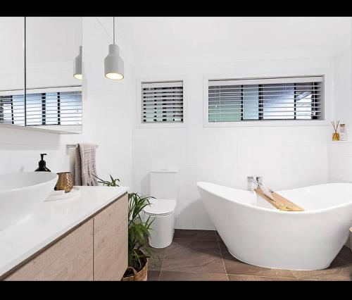 La salle de bains blanche est pourvue de 2 lavabos et d'une baignoire. dans l'établissement 5 bedroom Terrigal beach home with district views, à Terrigal