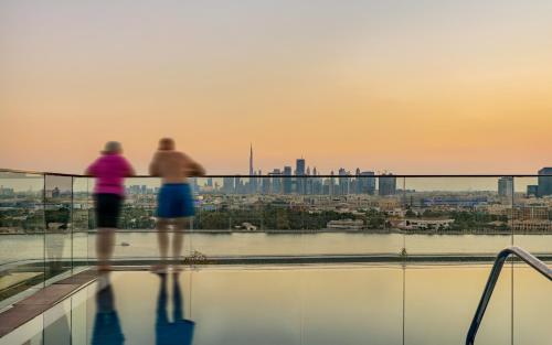 two people standing on the edge of a building overlooking a city at Al Bandar Arjaan by Rotana – Dubai Creek in Dubai