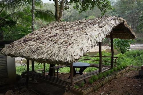 eine kleine Hütte mit einem Strohdach und einer Bank in der Unterkunft PONMUDI DALE. HOMESTAY in Kallar-Bridge
