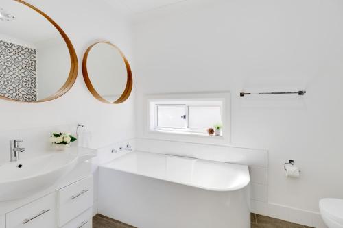 a white bathroom with a sink and a mirror at Modern Hamptons Cottage with Outdoor Deck in Mudgee