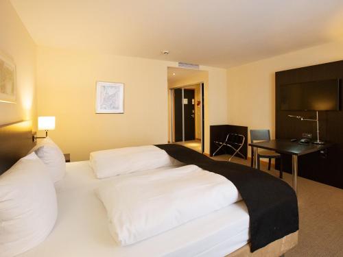 a hotel room with a bed with white sheets and a desk at DORMERO Hotel Altes Kaufhaus Lüneburg in Lüneburg