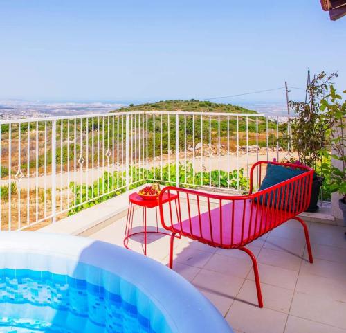 une terrasse avec une chaise rouge et une piscine dans l'établissement מול הים - בית נופש עם ממ"ד ומרפסת עם נוף פנורמי לים, à Moreshet