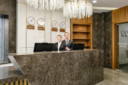 Ein Mann und eine Frau stehen an einer Theke in einer Lobby in der Unterkunft Grand Mildom Hotel in Almaty