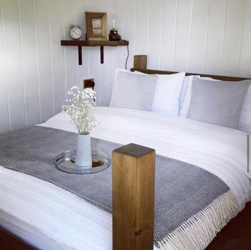 Una cama con una mesa con un jarrón de flores. en Trethowels Grey Hidden hut en St Austell