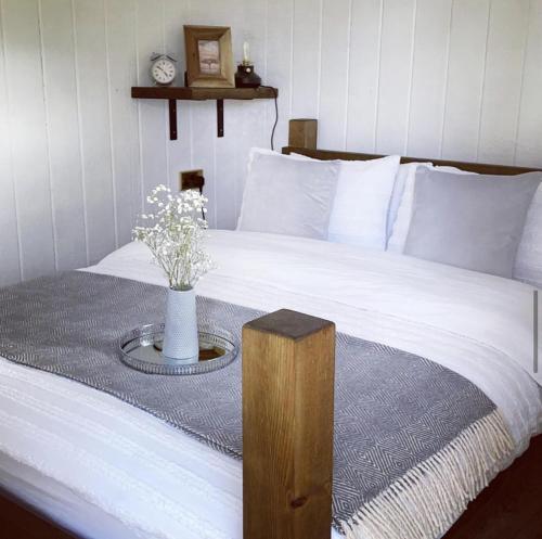 a bed with a table with a vase of flowers on it at Trethowels Grey Hidden hut in St Austell