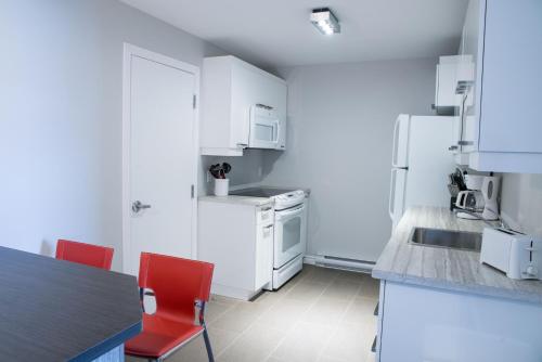 a kitchen with white appliances and red chairs at Le Chic-Urbain in Rouyn