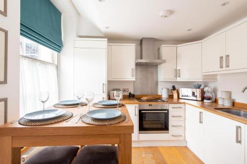 eine Küche mit weißen Schränken und einem Holztisch mit Tellern darauf in der Unterkunft Idyllic city centre apartment in Canterbury in Kent