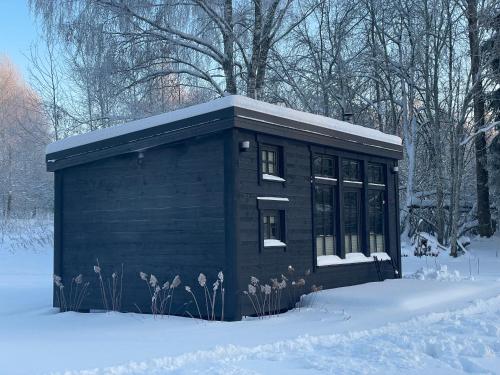 a small black building with snow on the ground at Ieviņi atpūtas vieta in Bānūži