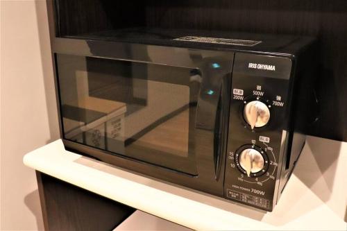 un horno de microondas negro sentado en un estante en Linore en Ginowan