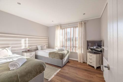 a white bedroom with two beds and a television at Waterfront Lodge Windsor Racecourse Marina in Windsor