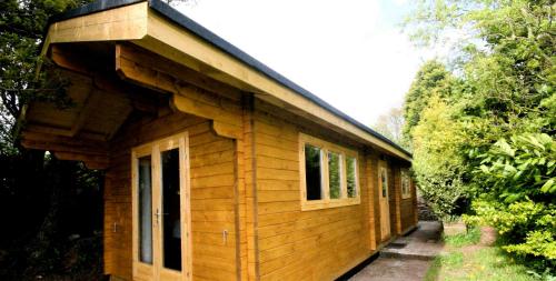a small wooden cabin with a gambrel roof at Yealm Cabin Self Catering Log Cabin in Devon with Hot Tub in Plymouth