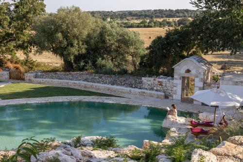 a woman sitting under an umbrella in a swimming pool at Masseria San Paolo Grande in Ostuni