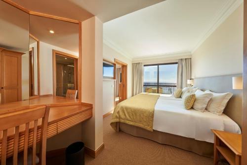 een slaapkamer met een bed, een bureau en een raam bij The Residence Porto Mare - PortoBay in Funchal