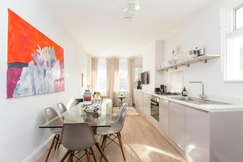 a white kitchen with a glass table and chairs at Newly renovated large 4/5 bedroom Victorian terrace house with garden. in London