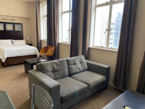a living room with a couch and a bed and windows at Mapungubwe Hotel Apartments Marshalltown in Johannesburg