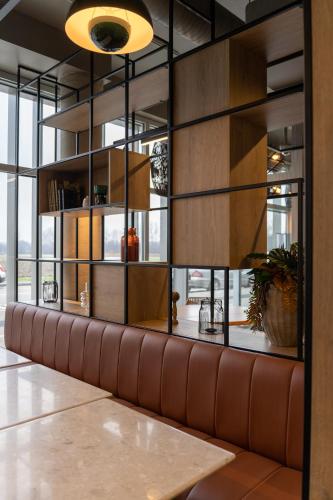 a brown leather bench in a room with windows at Ibis Bourgoin Jallieu Medipole in Bourgoin