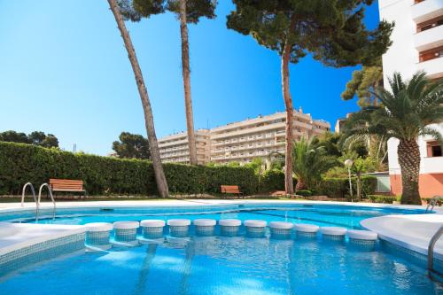 una piscina con palmeras y un gran edificio en UHC Buigas Luz Apartments, en Salou