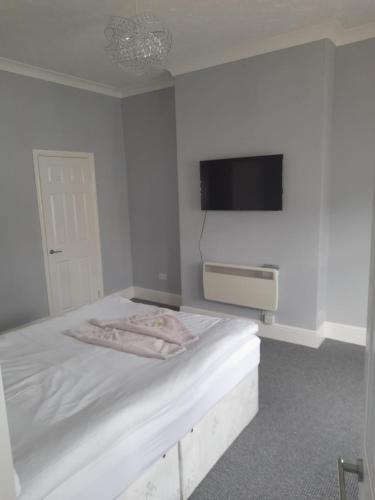 a white bedroom with a bed with a tv on the wall at VM Holiday let in Great Yarmouth