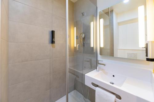 a bathroom with a shower and a sink and a mirror at B&B HOTELS Bourg-en-Bresse Viriat in Viriat