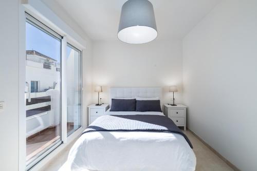 Dormitorio blanco con cama y ventana grande en Valle Romano Golf Resort Penthouse Apartmento, en Estepona