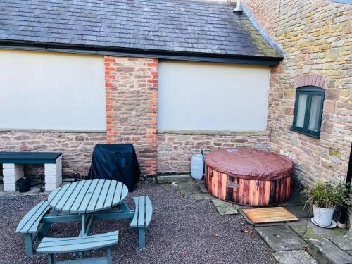 una mesa de picnic y un tronco de árbol al lado de un edificio en The Owl House Cottage, en Welsh Newton Common