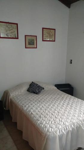 ein weißes Bett in einem Schlafzimmer mit zwei Bildern an der Wand in der Unterkunft La Casita in Santa Clara del Mar