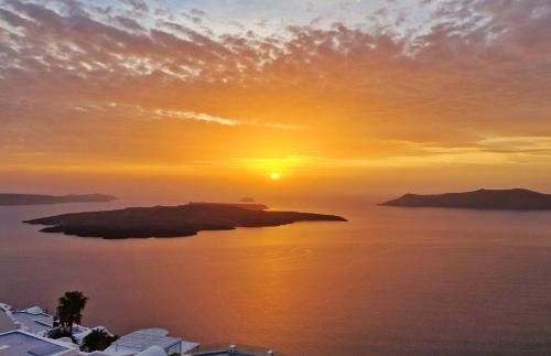 a sunset over a small island in the water at Karpimo Scenery in Firostefani