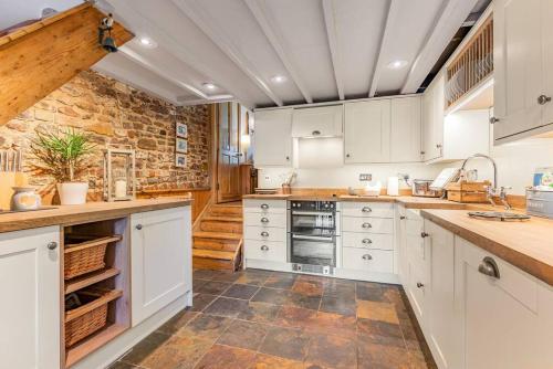 a kitchen with white cabinets and a stone wall at Pieman's Cottage - Pulborough, West Sussex Cottage - sunny courtyard in Pulborough