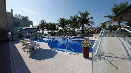una piscina con sillas, sombrilla y palmeras en Kaakupe Praia Hotel, en Guaratuba