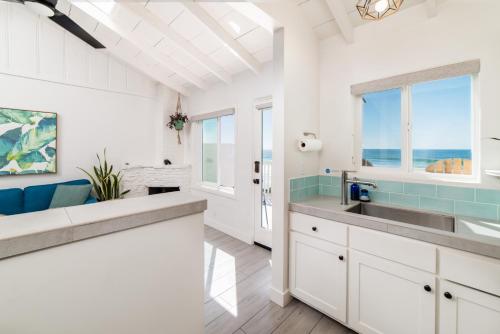 una cocina con armarios blancos, fregadero y ventanas en Pacific Villas en Oceanside