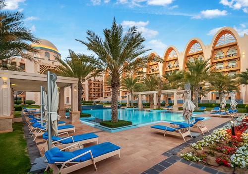 une piscine dans un complexe avec des chaises longues bleues et des palmiers dans l'établissement FAM Living - Beach Escapes in Palm Jumeirah, à Dubaï
