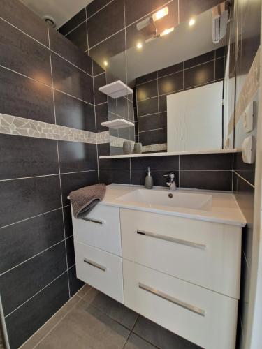 La salle de bains est pourvue d'un lavabo blanc et de carrelage noir. dans l'établissement Beness'Appart 5km Capbreton, à Bénesse-Maremne