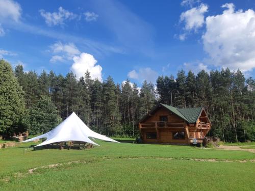 a tent in a field next to a log cabin at Poilsio ir sveikatinimo sodyba Pušų Šlamesy in Vilnius