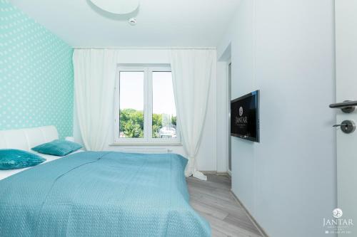 sypialnia z niebieskim łóżkiem i oknem w obiekcie Jantar Apartamenty - Boutique Polanki Park SPA w Kołobrzegu
