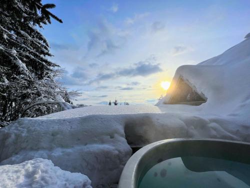 una bañera de hidromasaje cubierta de nieve con el sol al fondo en Cottage House Jakob, en Cerklje na Gorenjskem