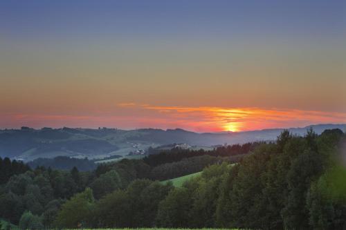 a sunset over a valley of trees with the sun setting at Curhaus Bad Kreuzen in Bad Kreuzen