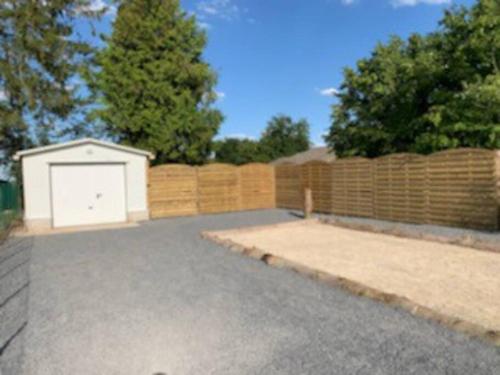 a driveway with a white garage in front of a fence at Gîte Au Crépuscule du Belvédère in Dompierre-Becquincourt