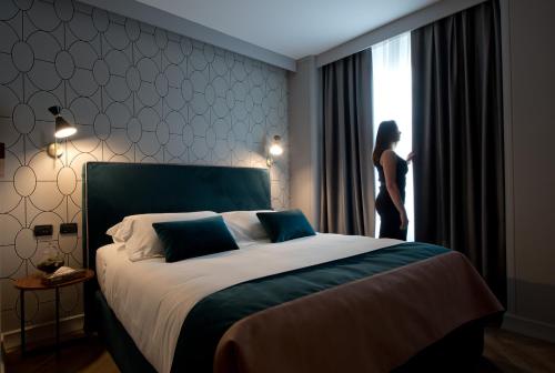 Eine Frau, die in einem Schlafzimmer steht und aus dem Fenster schaut. in der Unterkunft Duomo Hotel & Apartments in Mailand