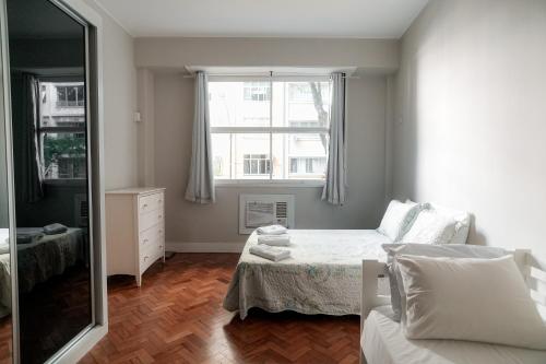 1 dormitorio con cama, ventana y espejo en Apartamento confortável na quadra da praia, en Río de Janeiro
