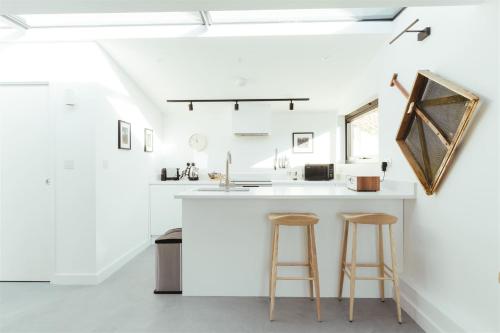 a kitchen with a white counter and two stools at The Hopper Huts in Faversham