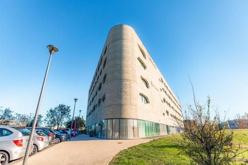 a tall building with cars parked in a parking lot at Appart’City Confort Montpellier Millénaire in Montpellier