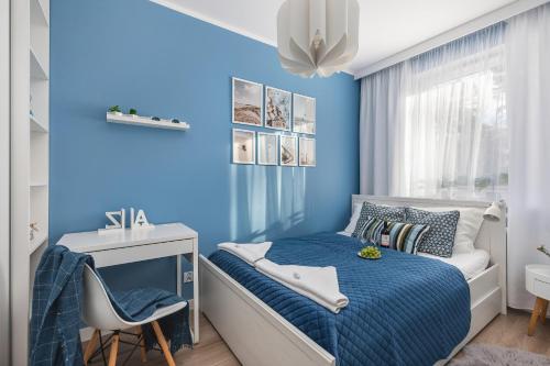 a blue bedroom with a bed and a desk at Apartment Leśne Tarasy Dziwnówek by Renters in Dziwnówek