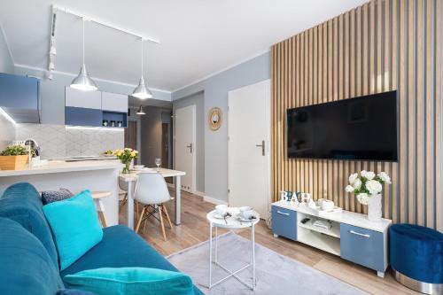 a living room with a blue couch and a kitchen at Apartment Leśne Tarasy Dziwnówek by Noclegi Renters in Dziwnówek