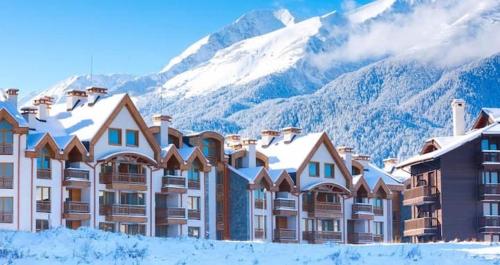 a hotel with snow covered mountains in the background at Studio Chalet 13, St John Park Bansko in Bansko