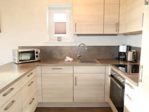 eine Küche mit Holzschränken, einer Spüle und einer Mikrowelle in der Unterkunft Holiday Home Trottellumme by Interhome in Dagebüll