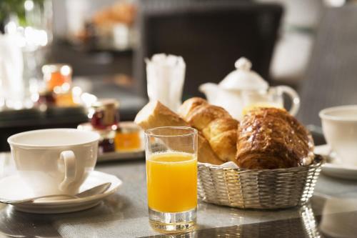 a glass of orange juice next to a basket of pastries at Hotel du Champ de Mars in Paris