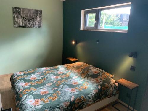 1 dormitorio con 1 cama con colcha de flores y ventana en Le cabanon, en Houffalize